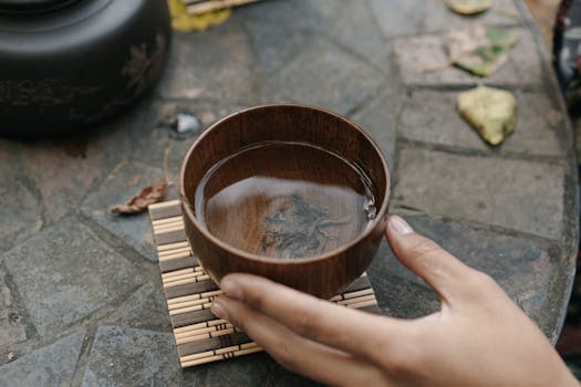 Close-up of a hand holding a traditional wooden tea bowl during a tea ceremony.