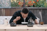 A young man enjoys ramen outdoors, using chopsticks on a rustic table setting.