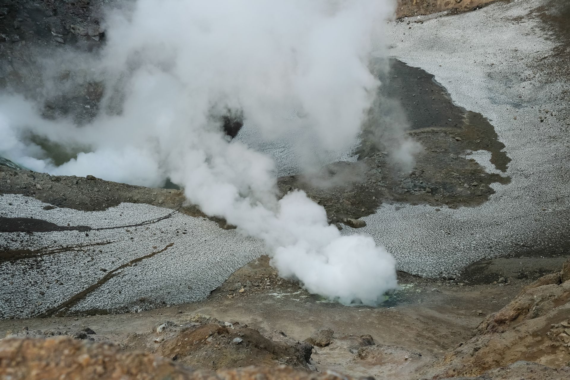 Aerial view of a steaming crater in a volcanic geothermal area with visible steam vents.