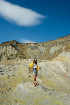 Woman hiking with trekking poles in rugged desert mountains under a blue sky.