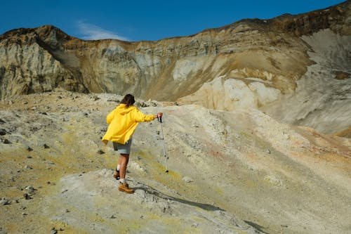 Man in Yellow Shirt and Blue Shorts Holding Stick Standing on Rocky Hill
