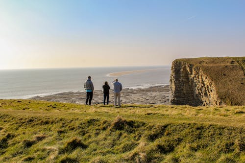 Three People On Top Of Hill Near Body of Water