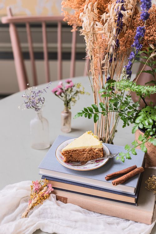 Free Slice of cake with cinnamon sticks on books, surrounded by wildflowers indoors. Stock Photo