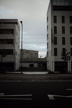 A quiet urban street flanked by modern buildings under a cloudy sky.