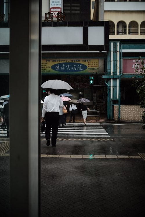 Free Pedestrians with umbrellas crossing a wet city street on a rainy day, reflecting urban life. Stock Photo