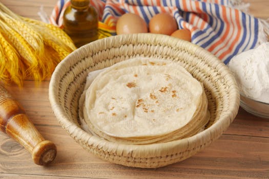 Close-up of traditional roti flatbread in a woven basket with ingredients on a wooden surface.