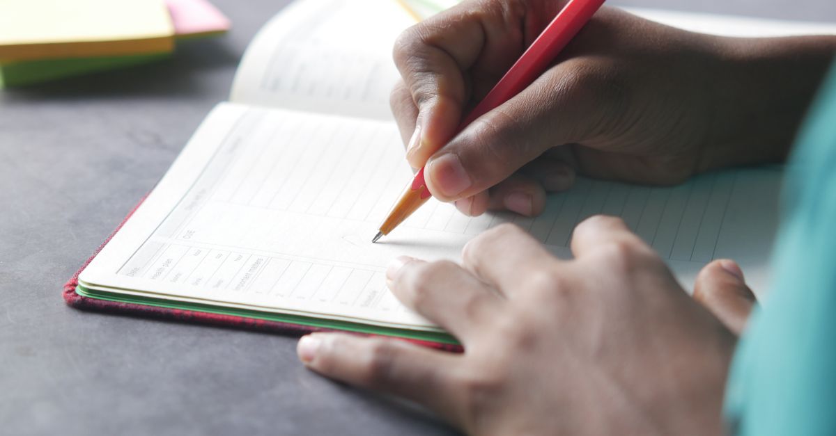 Close-up of a hand writing in a notebook with a pencil indoors.