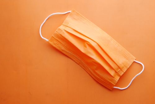 Free Close-up of an orange surgical mask on orange background, highlighting PPE and pandemic theme. Stock Photo