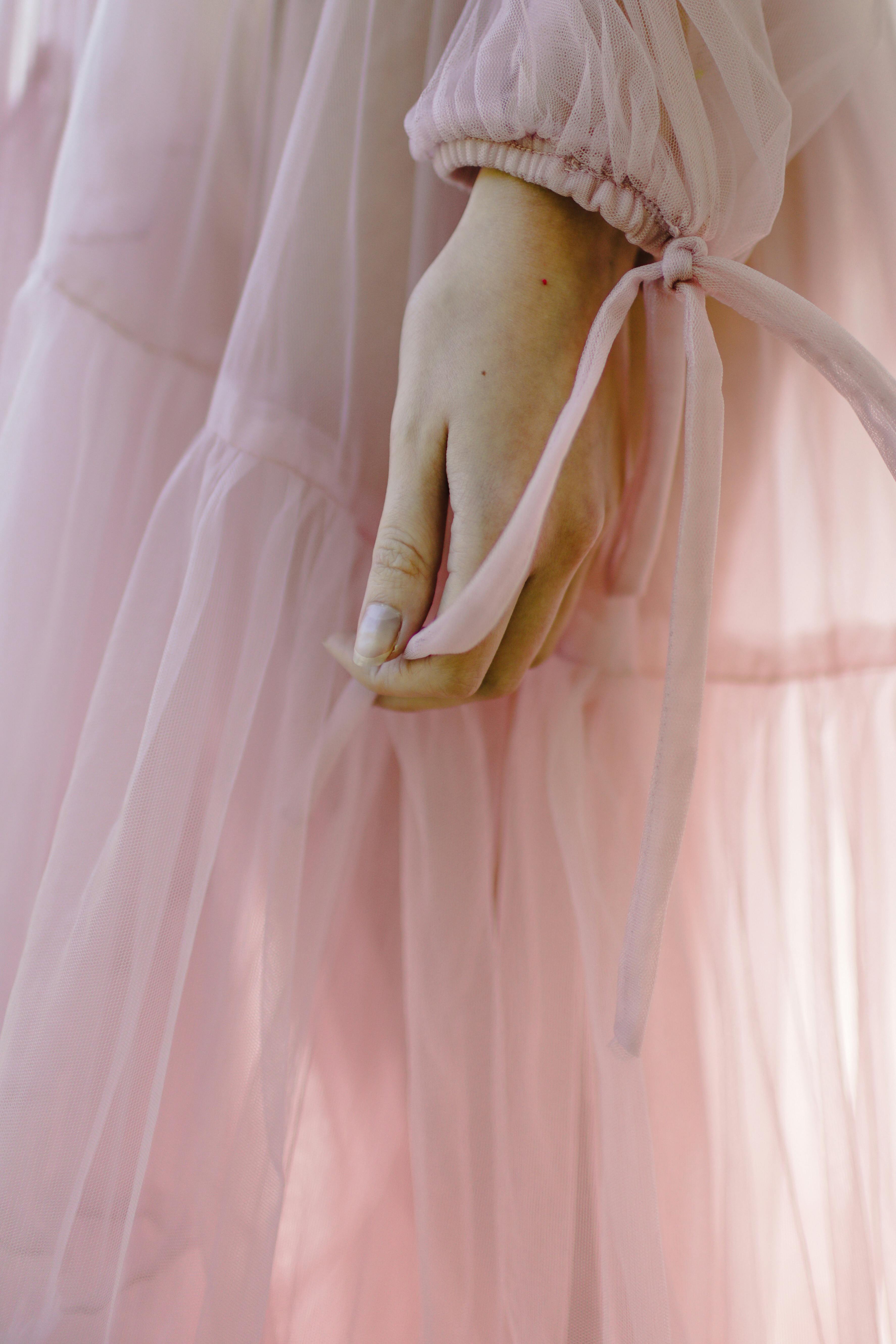 A delicate hand gracefully stands out in a soft pink dress, highlighting elegance and style.