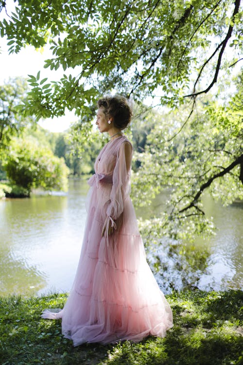 Free Woman in Pink Dress Standing on Grass Near Lake Stock Photo