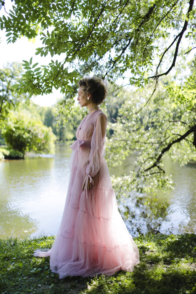 Woman In Pink Dress Standing On Grass Near Lake