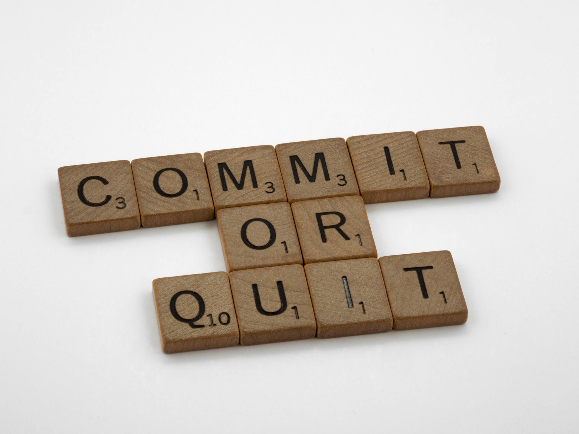 Wooden Scrabble tiles arranged to form the words 'Commit or Quit' on a white background.