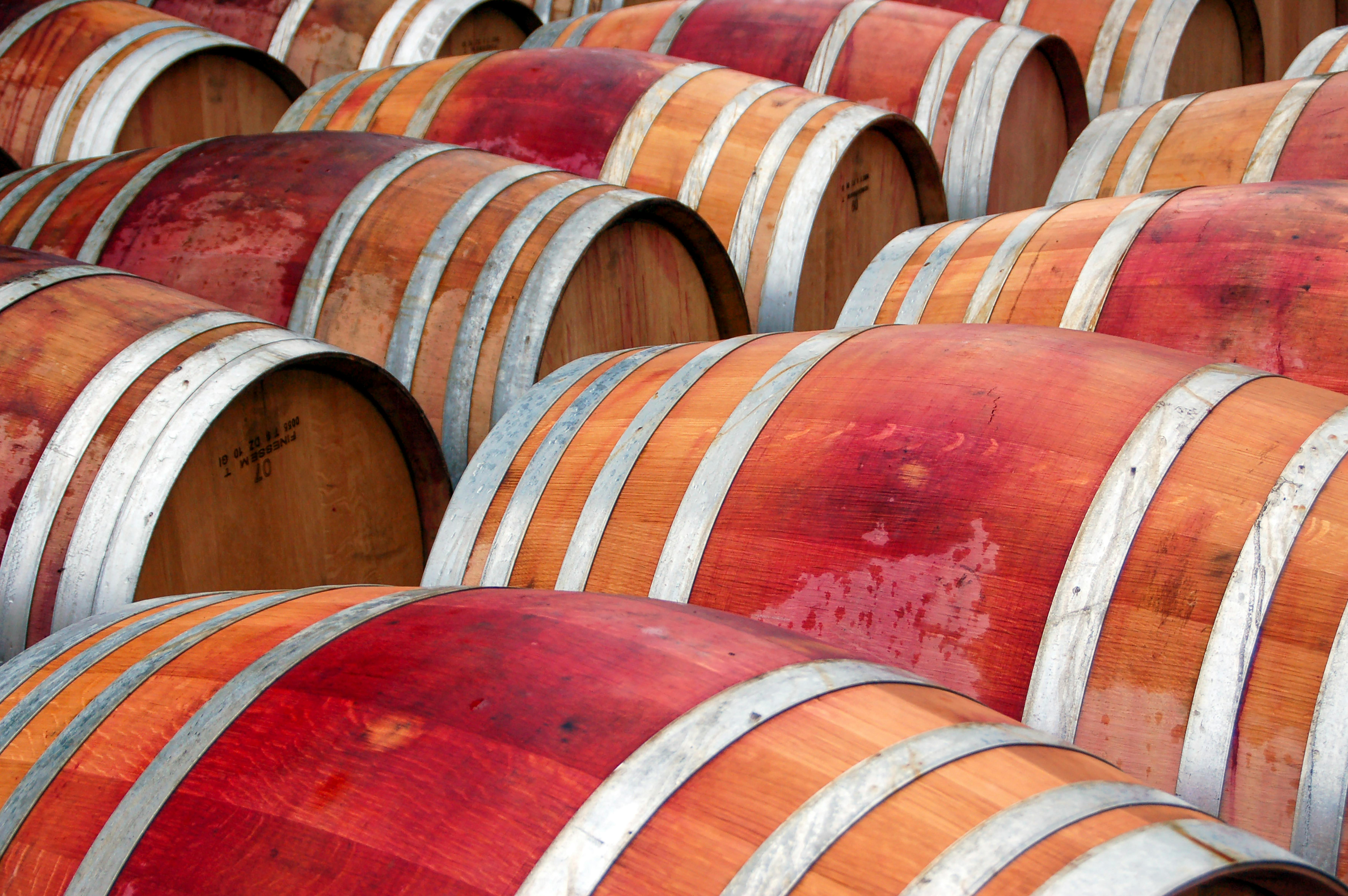 Close-up of multiple wooden wine barrels in a cellar, showing rustic texture.