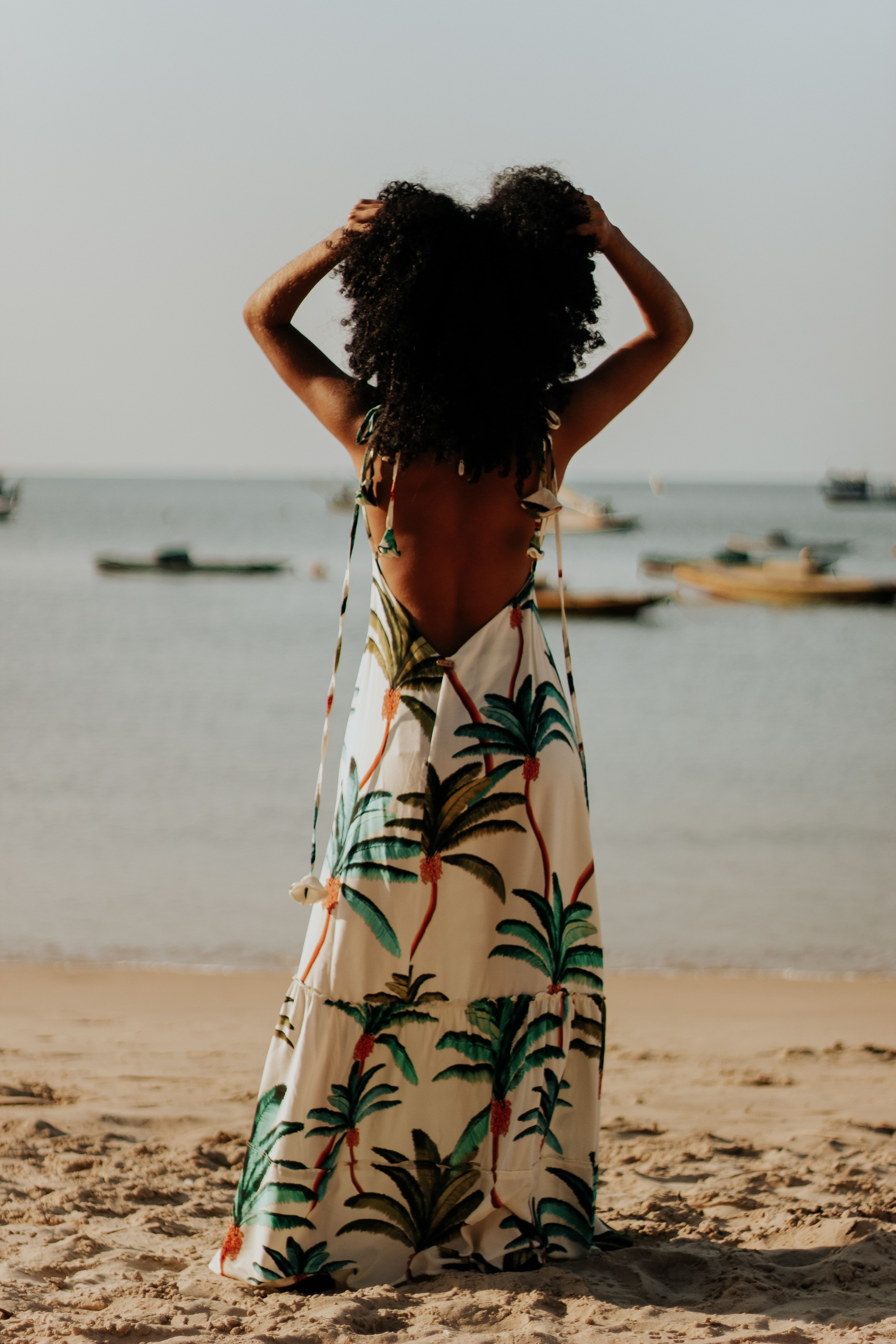African American woman in a tropical dress standing on a sunny Brasil beach with a serene ocean view.