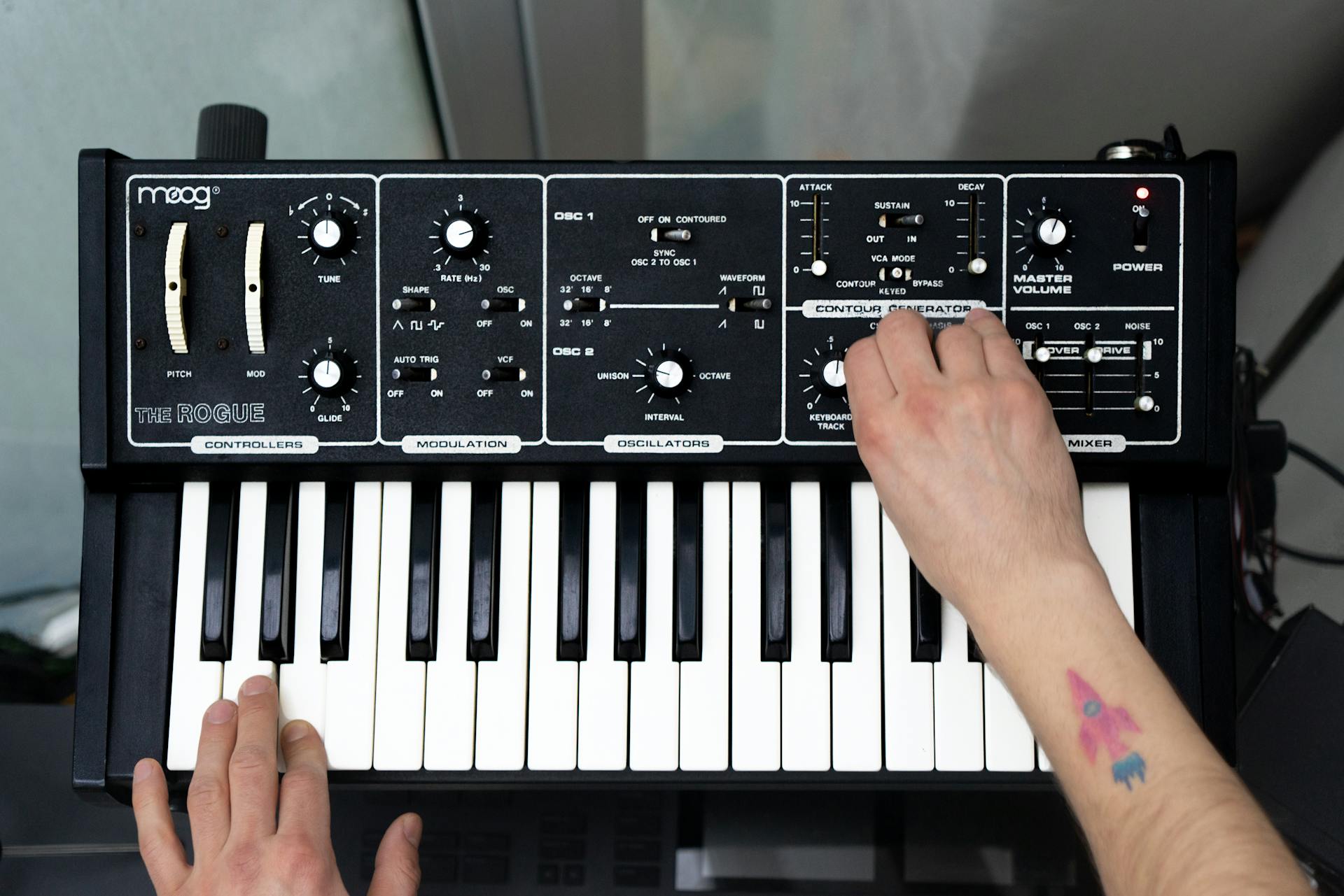 A person playing a Moog synthesizer with both hands visible, showing the control panel and keyboard.