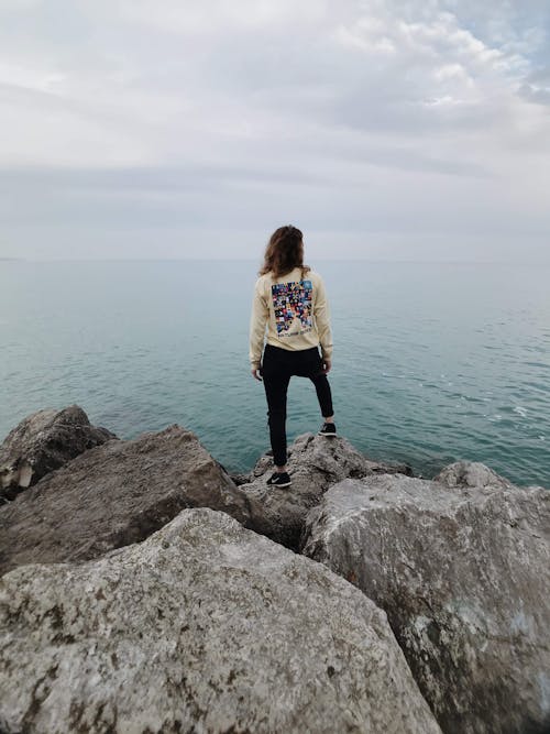 Free A Woman Standing on a Rock by a Sea Stock Photo