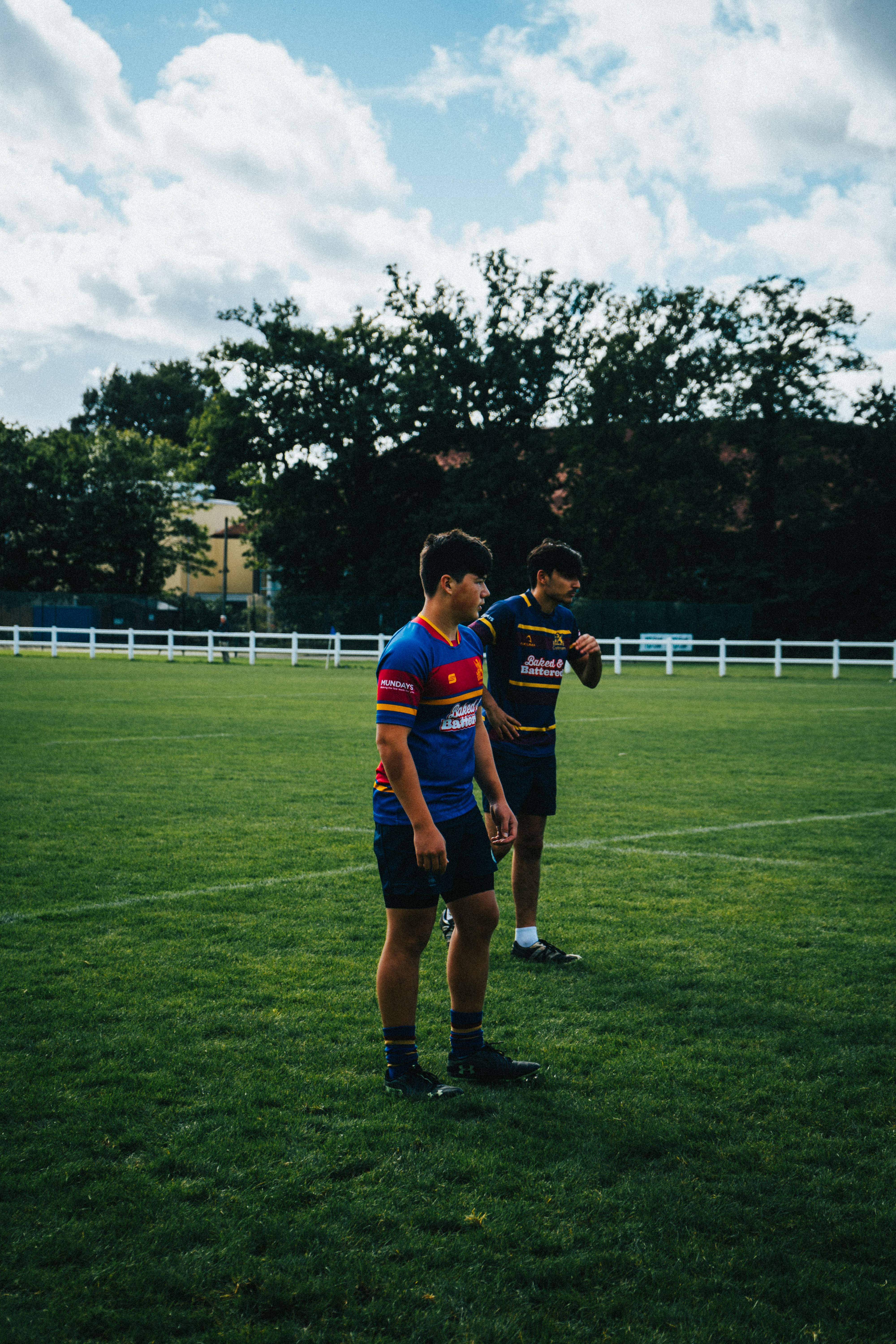 Two rugby players stand on a grassy field, ready for action.
