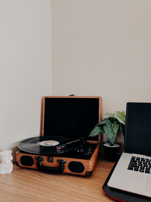 Free A vintage turntable and laptop on a minimalist wooden desk, adding a retro touch to a modern workspace. Stock Photo