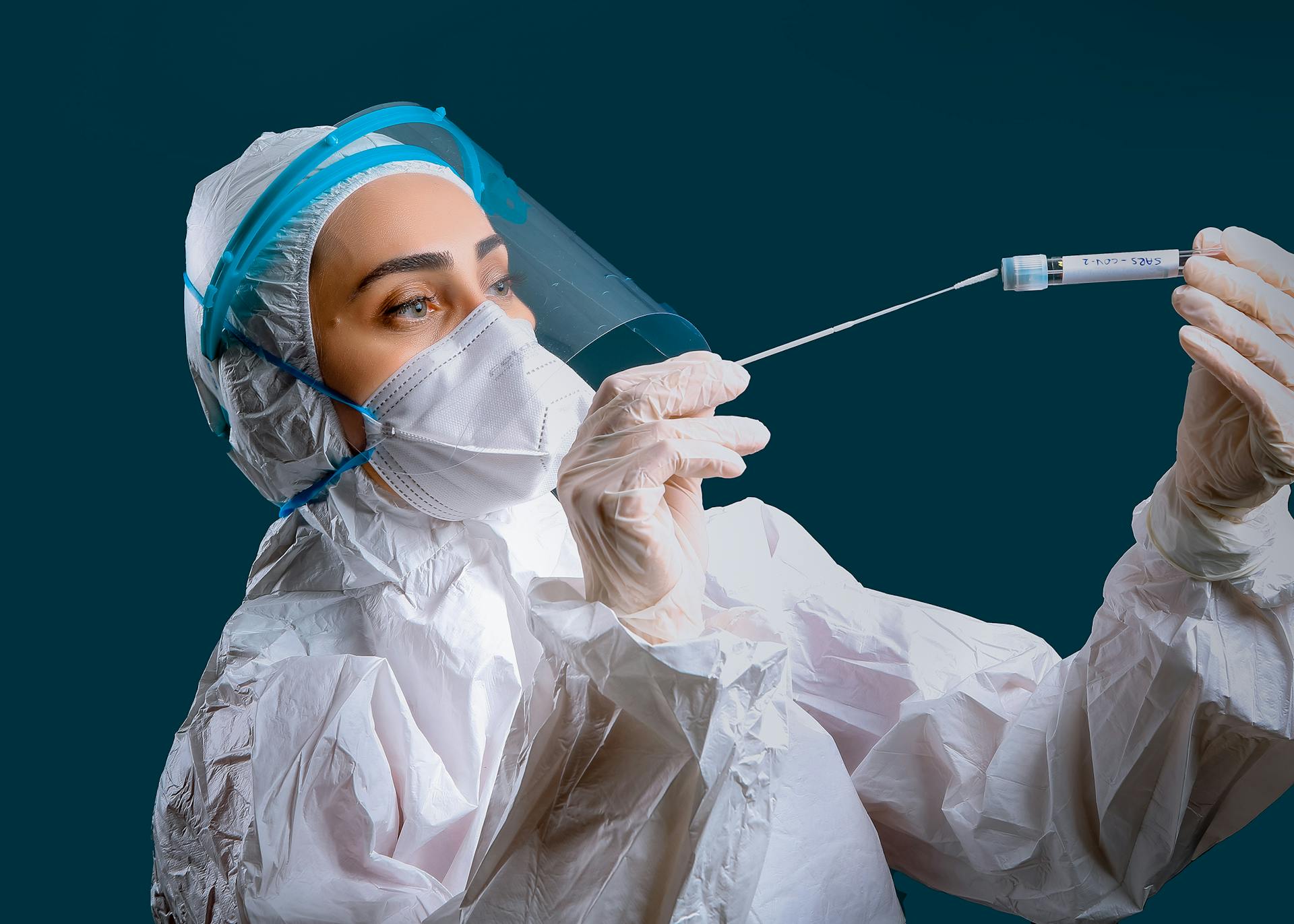 A healthcare worker in full PPE holding a test swab, representing health safety and virus testing.