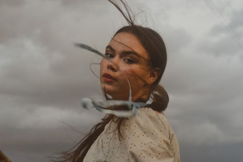 Free Artistic portrait of a woman with wind-swept hair against a dramatic cloudy sky. Stock Photo