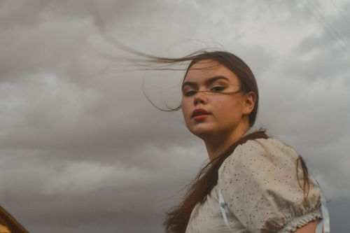 Free Artistic portrait of a young woman with wind-swept hair under an overcast sky, expressing beauty and emotion. Stock Photo