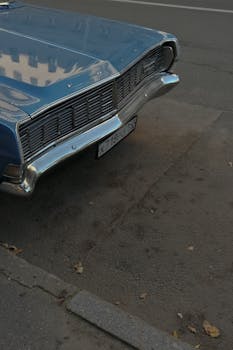 Close-up of a vintage blue car parked on an urban street, showcasing its shiny grille and retro design.