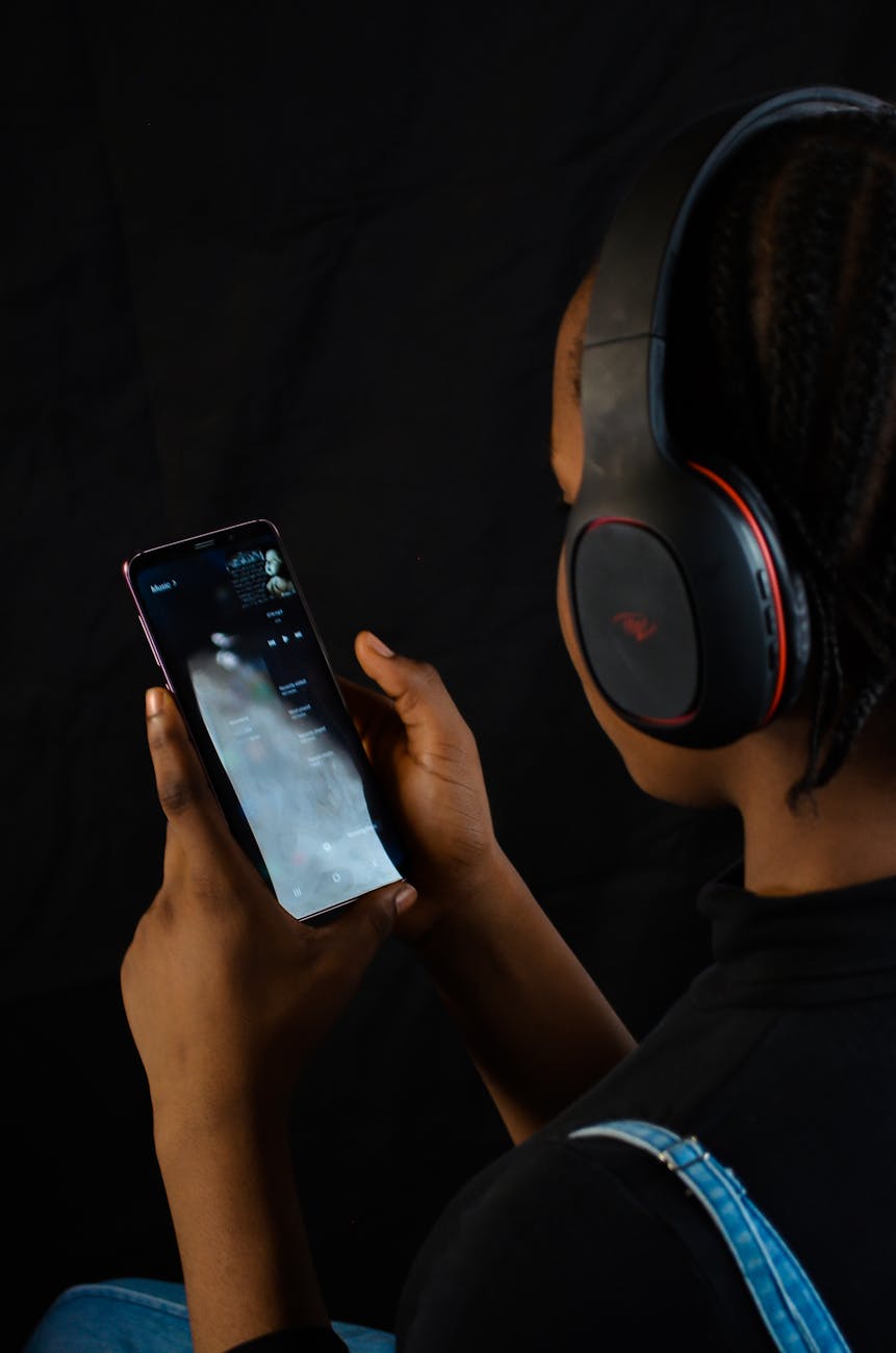 Adult holding a smartphone and using wireless headphones indoors, creating a tech-savvy mood.
