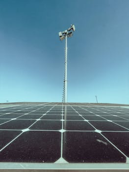Solar panels under a clear blue sky with a communication tower in the background.
