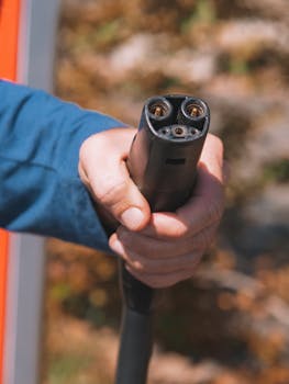 Close-up shot of a hand holding an electric vehicle charger, symbolizing clean energy.