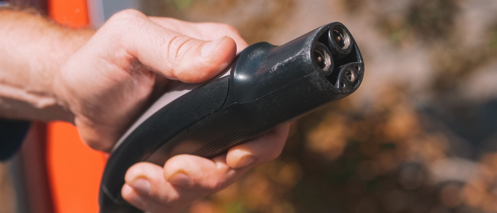 Hand holding an electric vehicle charging plug, symbolizing clean energy and innovation.