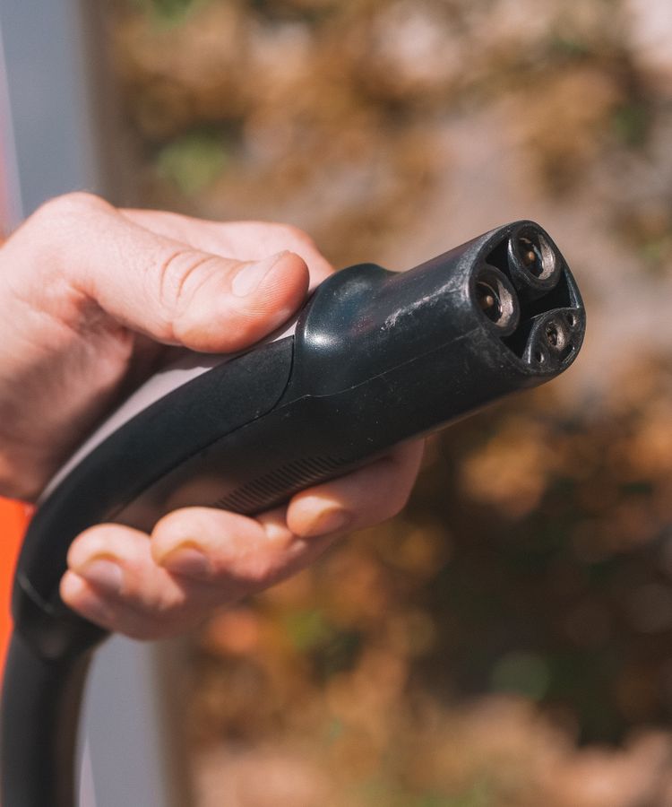 Hand holding an electric vehicle charging plug, symbolizing clean energy and innovation.
