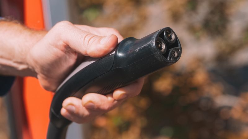 A driver plugging a heavy black charging cable into a modern electric car at an outdoor commercial charging station