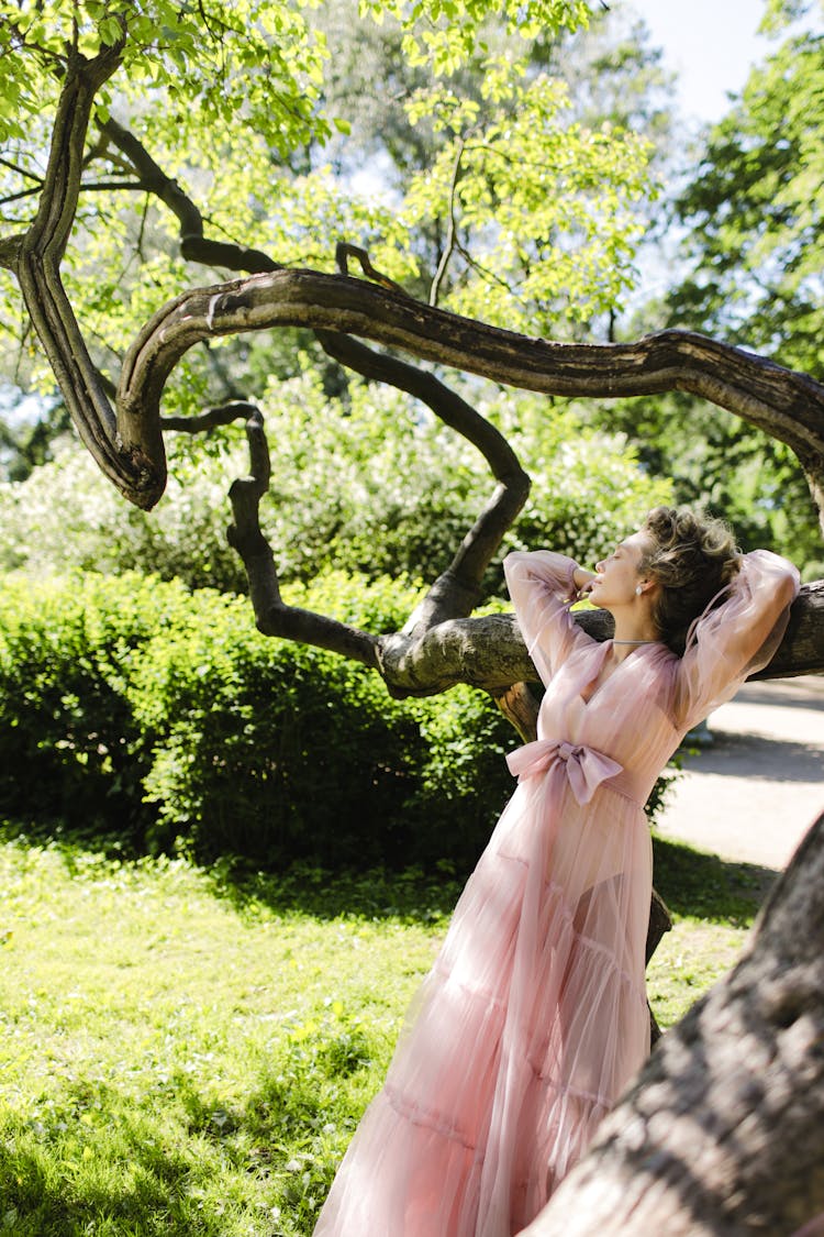 Woman Wearing Long Dress Leaning On A Tree Branch