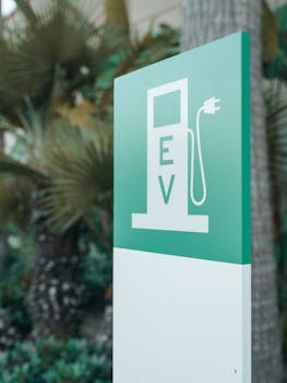 Close-up of a green and white electric vehicle charging station sign with nature background.