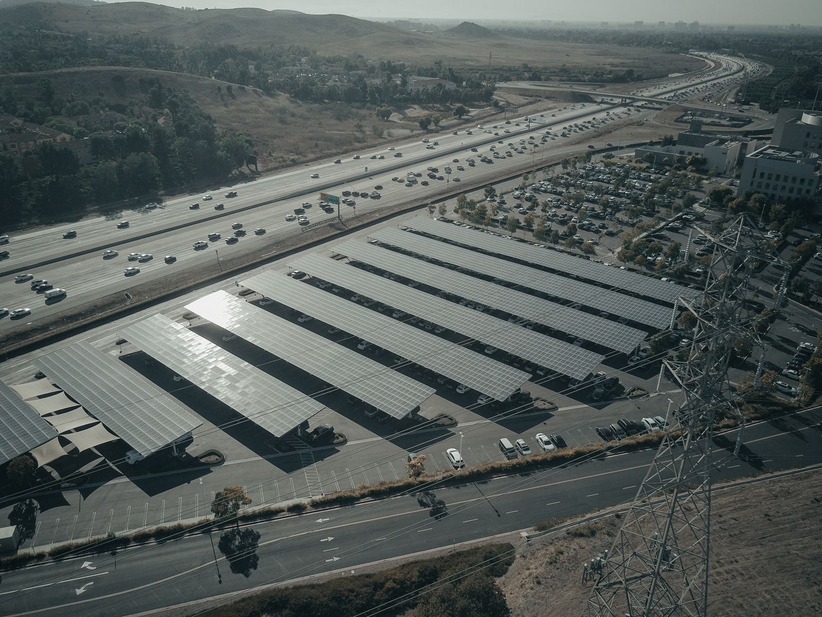 Aerial view of solar carport rows covering a highway-adjacent EV parking lot