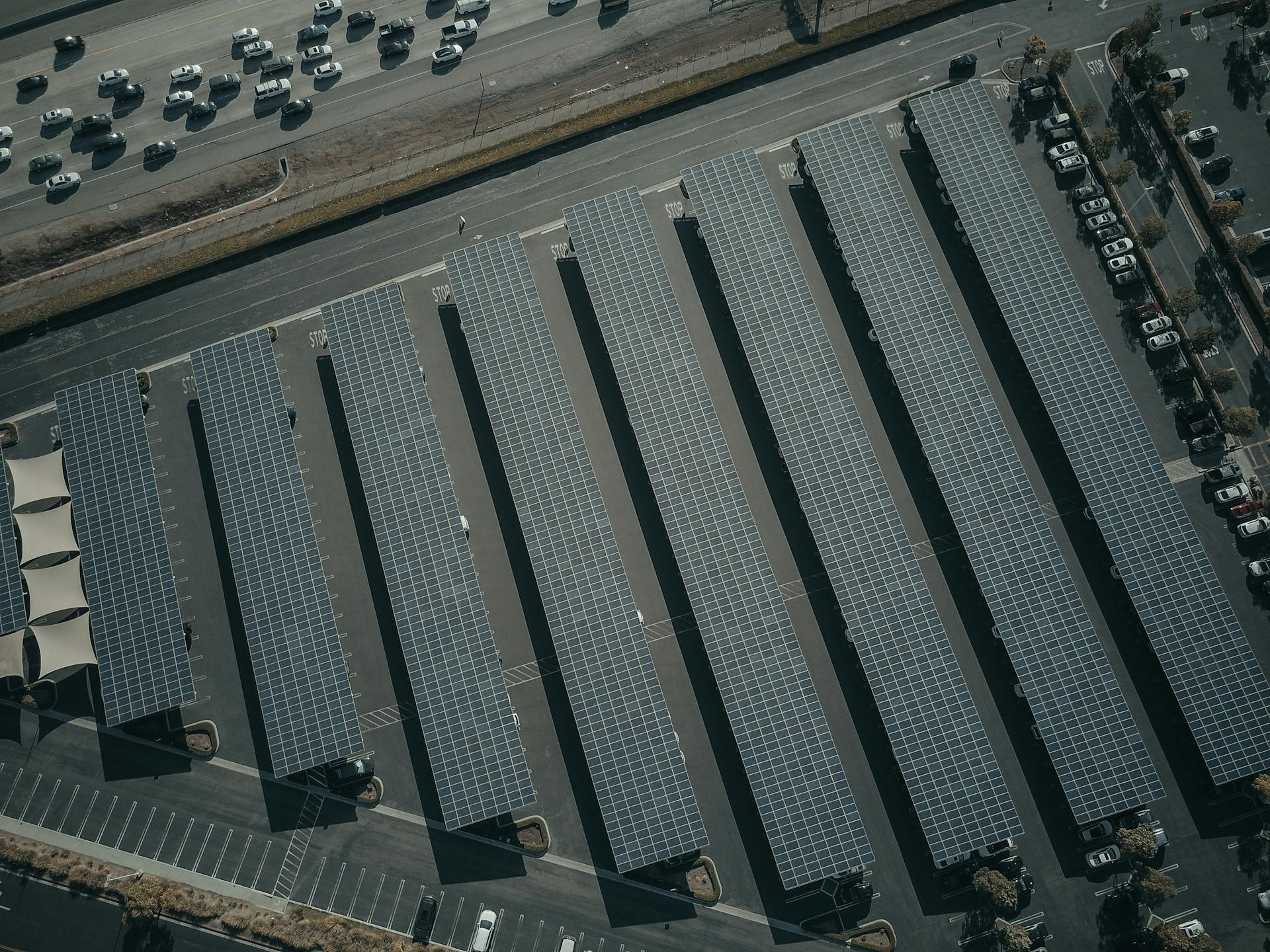 An aerial view showcasing a solar farm with aligned solar panels next to a busy parking lot.