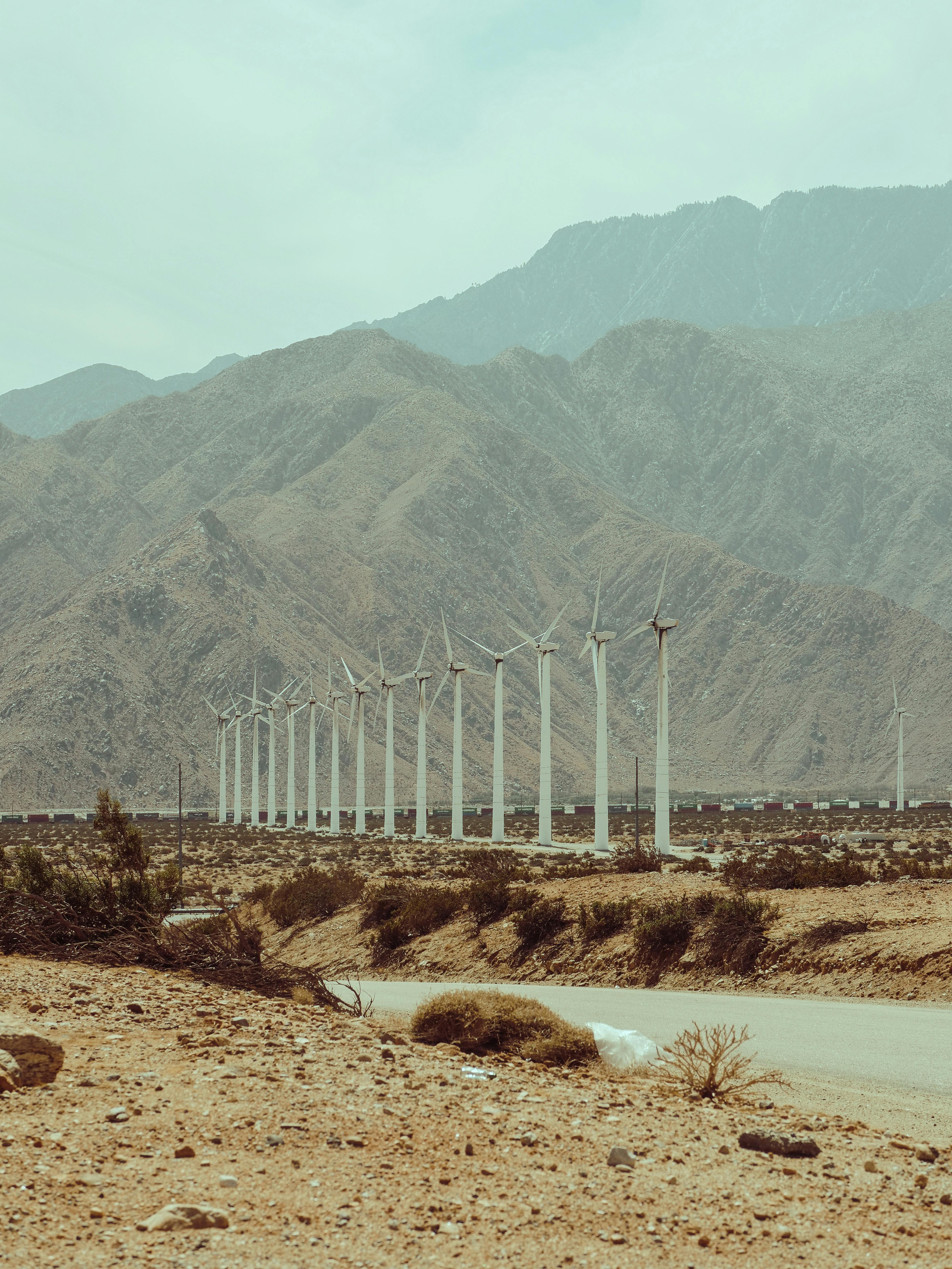 Line of wind turbines in a desert landscape with mountains under a clear sky, symbolizing renewable energy.