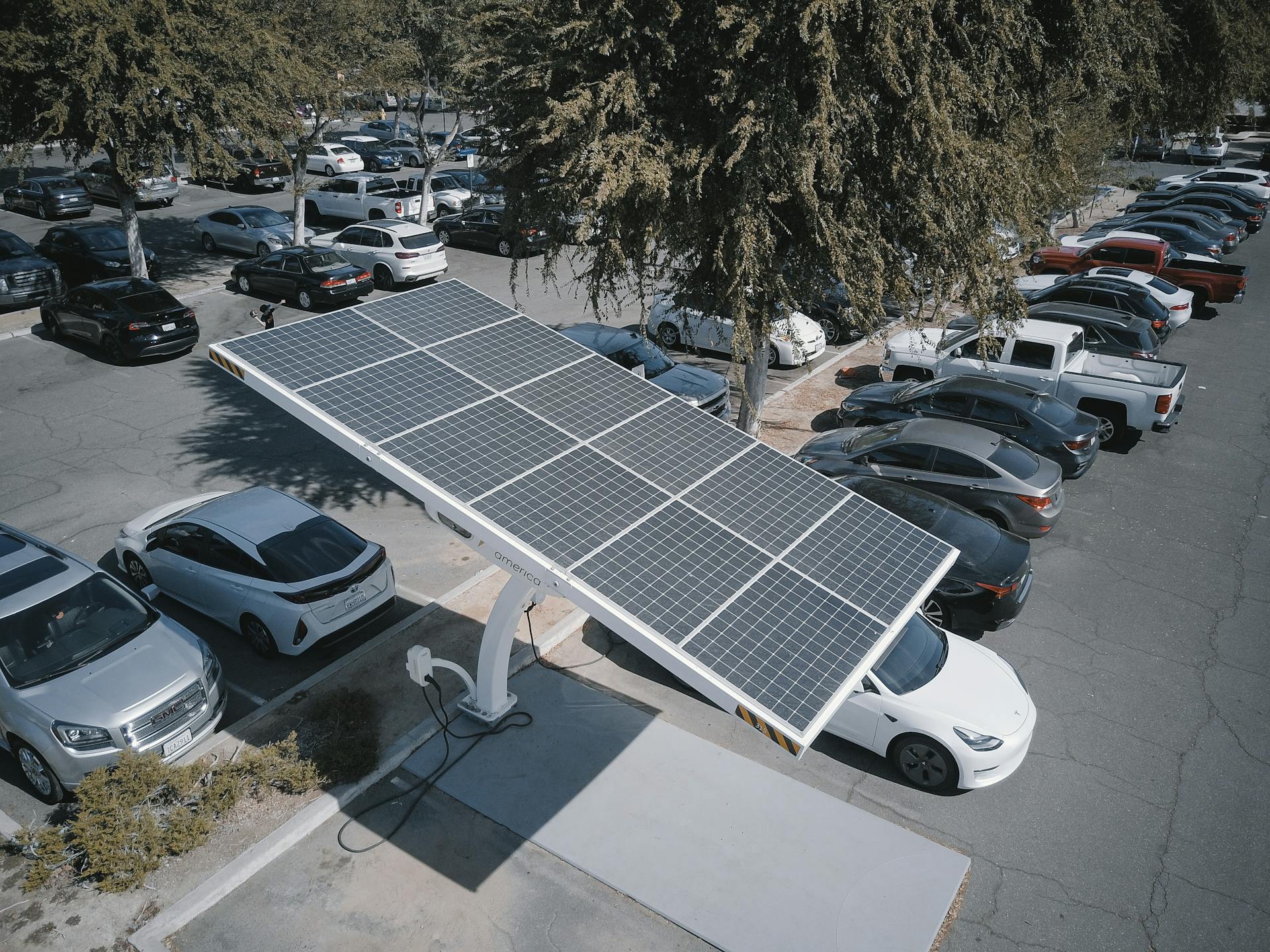 Electric cars charging at a solar-powered station in a parking lot.