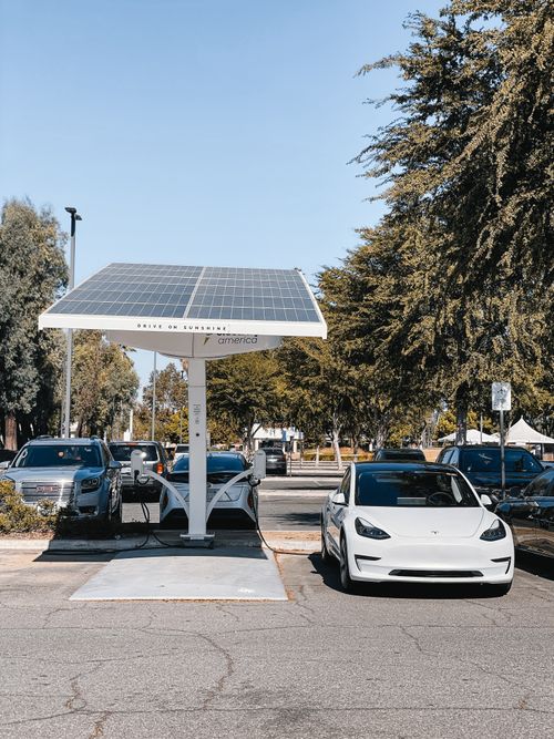 Free A white electric car charging under a solar panel in an urban setting, showcasing renewable energy use. Stock Photo