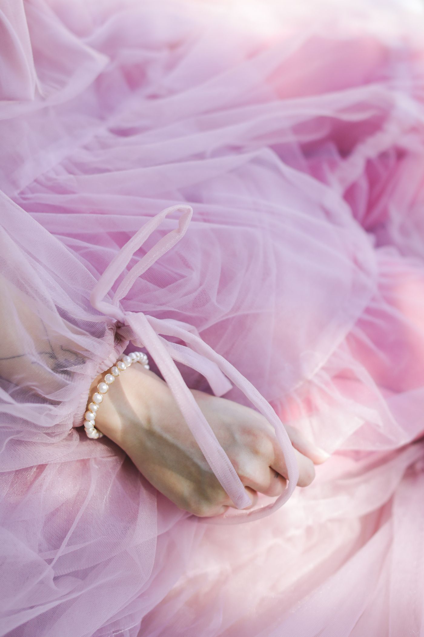 The hand of a woman in a pink dress — styling a blush dress with delicate gold jewellery
