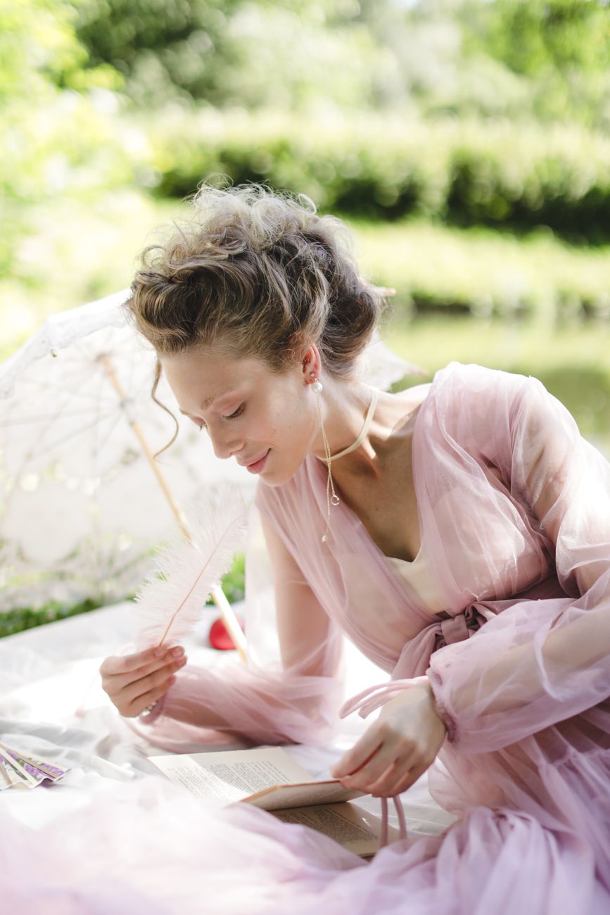 A woman in a pink dress enjoys a serene garden picnic with an umbrella and book.