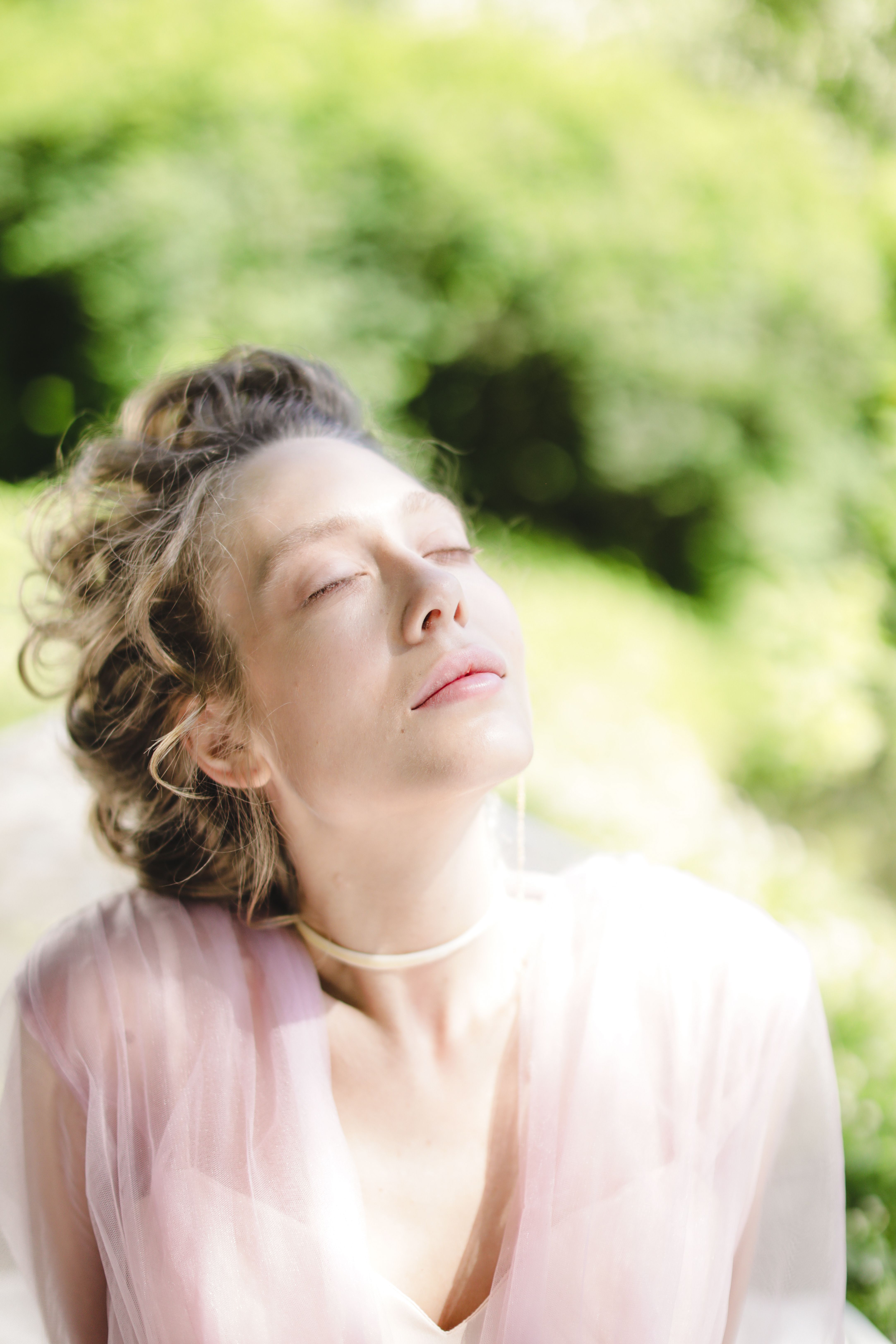 Portrait of a woman in a pink dress with closed eyes, captured in natural light outdoors.