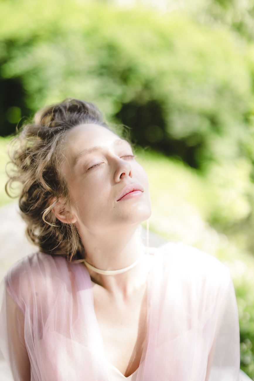 Portrait of a woman in a pink dress with closed eyes, captured in natural light outdoors.