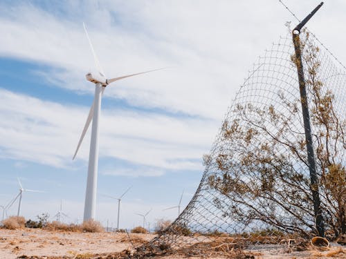 Broken Mesh Fence on Desert with Wind Turbines