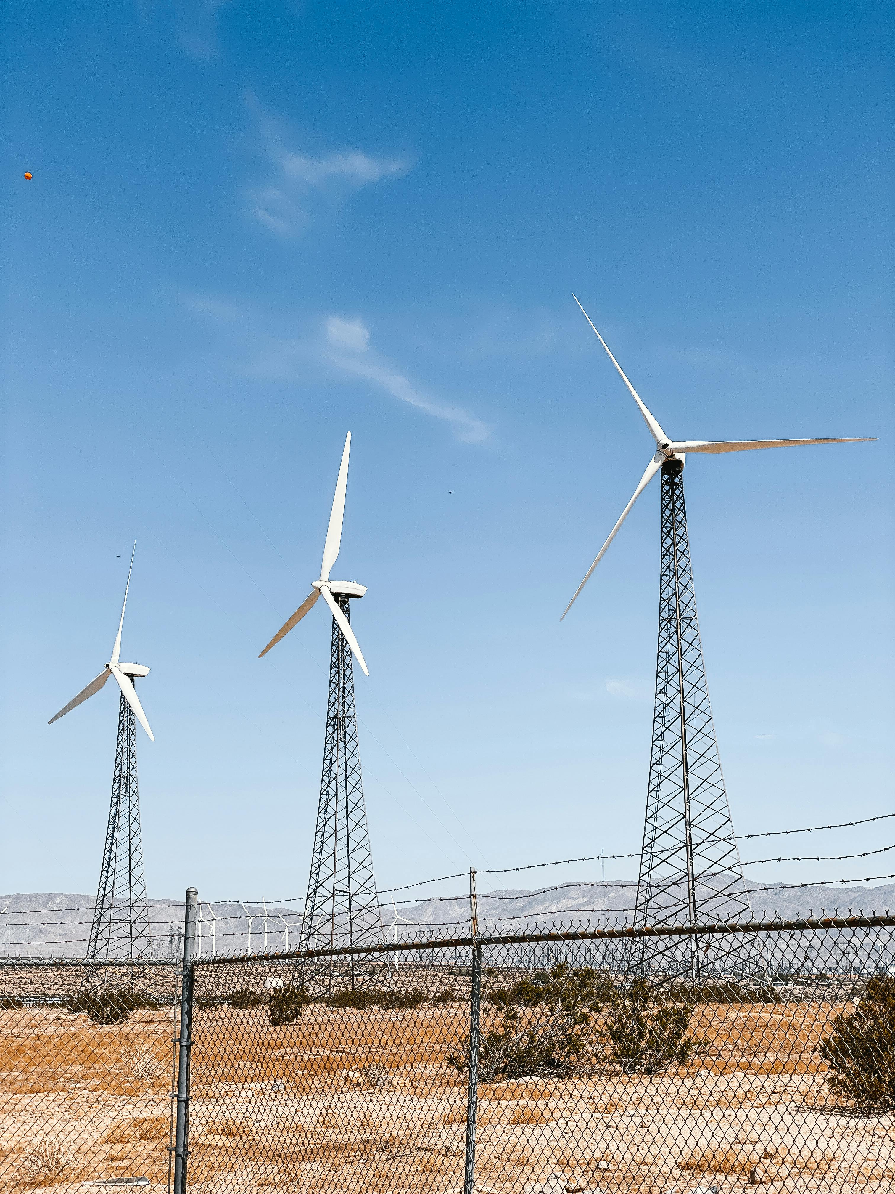 Three wind turbines generating clean energy in a desert setting with clear blue skies.