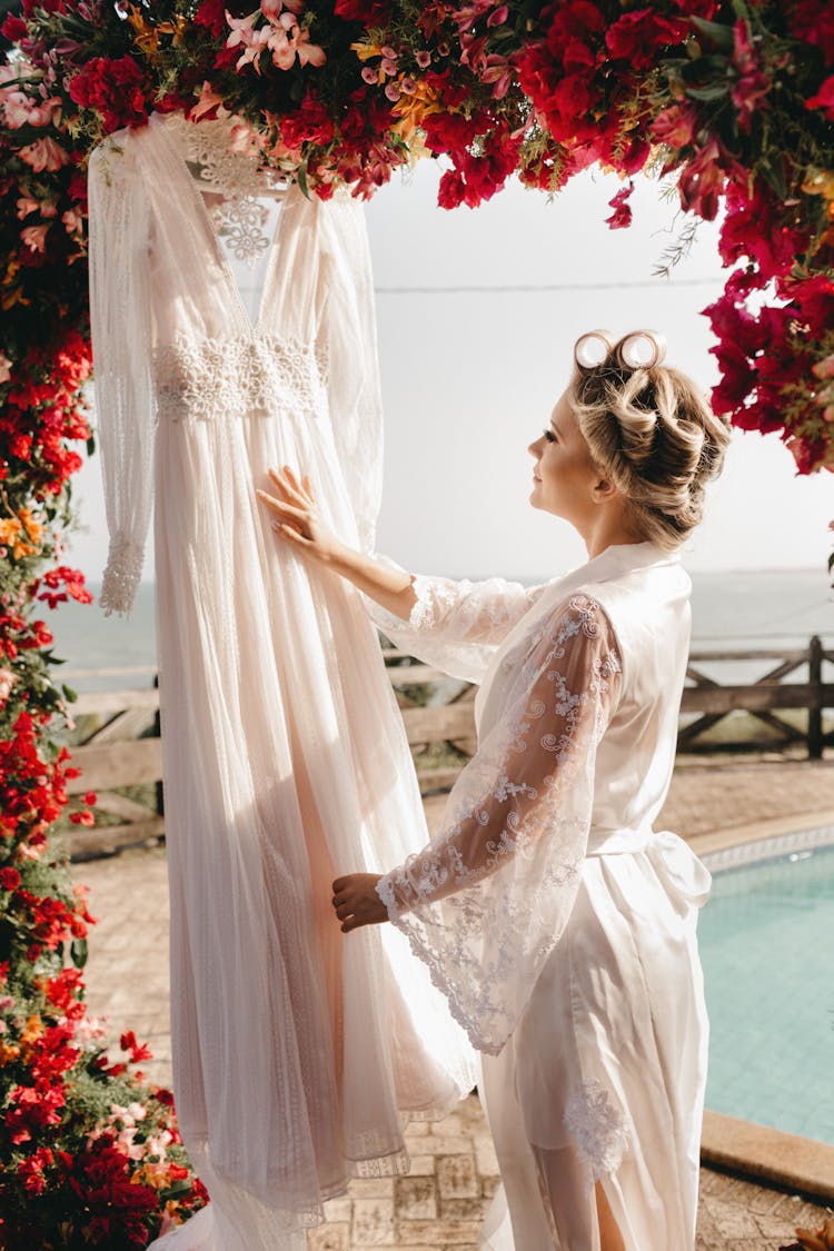 Woman In White Dress Touching Dress Hanging From Flower Arch