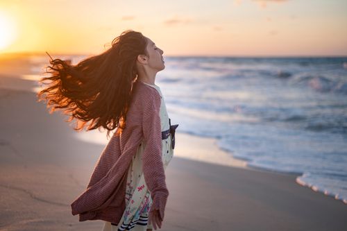 Free A woman with flowing hair stands on the beach at sunset, enjoying the serene ocean view. Stock Photo