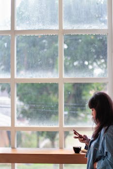 雨天，一名女子在咖啡馆的大窗户旁使用智能手机