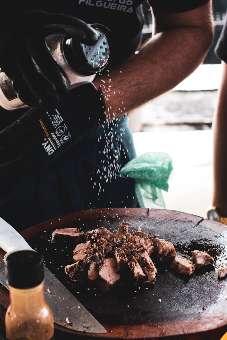 Person Putting Salt On Grilled Pork