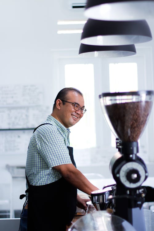 Man Wearing Plaid T-shirt And Black Apron in Front of Coffeemaker